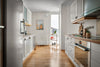 A narrow kitchen with white cabinets and wood floors
