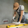 A person in a cap and overalls cutting a tile with an angle grinder