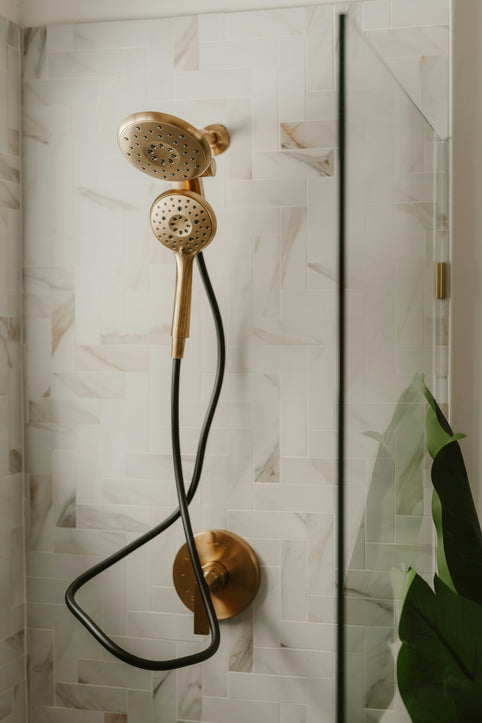 Gold shower head with black hose in modern bathroom.
