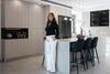 A woman stands in a modern, well-lit kitchen.