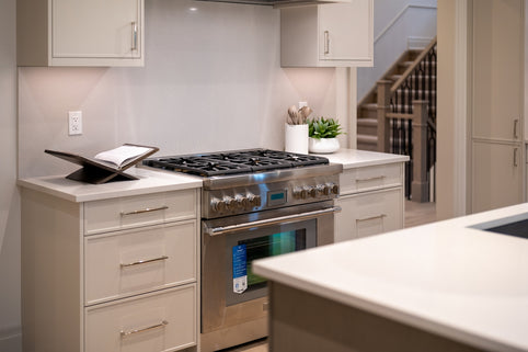 Modern kitchen with stainless steel stove, light cabinets, and cookbook.