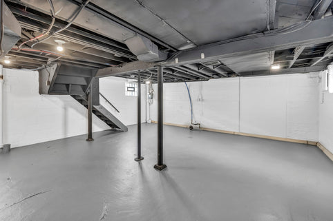 Spacious unfinished basement with exposed joists, support poles, and stairs.