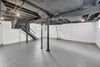 Spacious unfinished basement with exposed joists, support poles, and stairs.