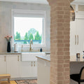 Modern kitchen with white cabinets, farmhouse sink, and brick pillars.