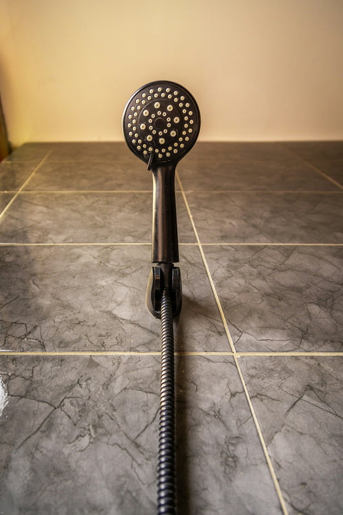 Black shower head with hose against a tiled wall.